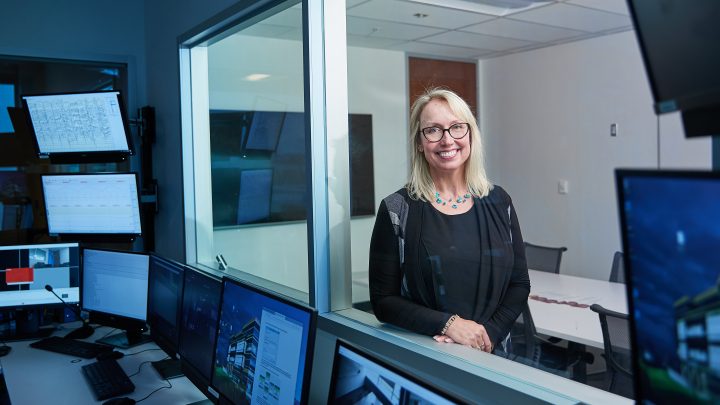 Photo of Dr. Milena Head in a window of a lab space with computer monitors